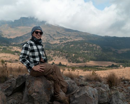 Free A hiker sitting on a rock with a camera in a scenic mountain landscape. Stock Photo