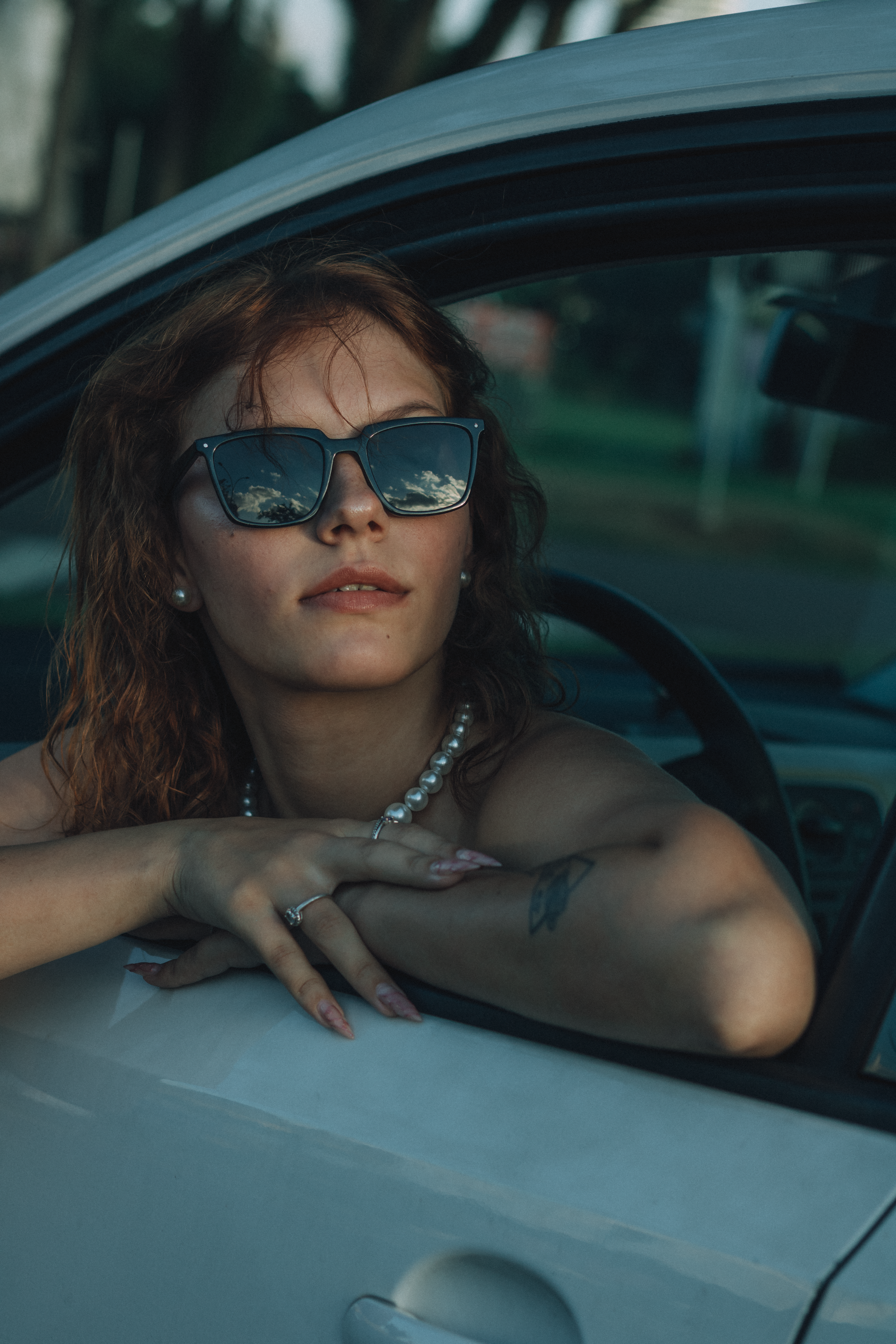 Woman wearing sunglasses leaning out of car window, looking relaxed.