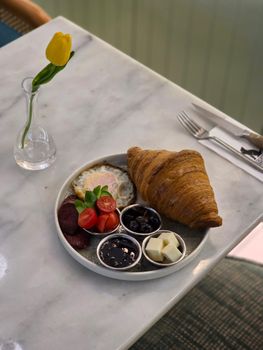 A delicious continental breakfast with croissant, eggs, and toppings on a marble tabletop.