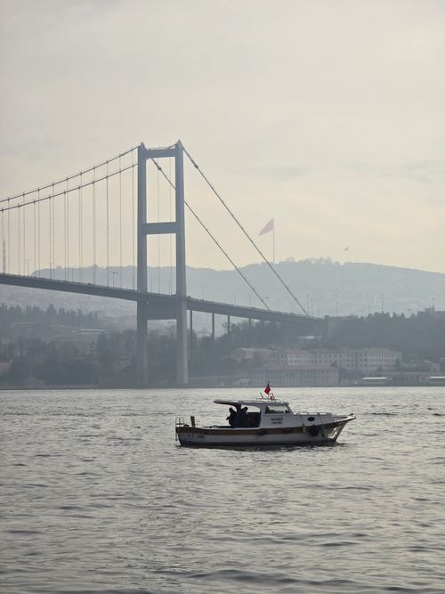 Free Boat on the Bosphorus with the Fatih Sultan Mehmet Bridge in the background, misty atmosphere. Stock Photo