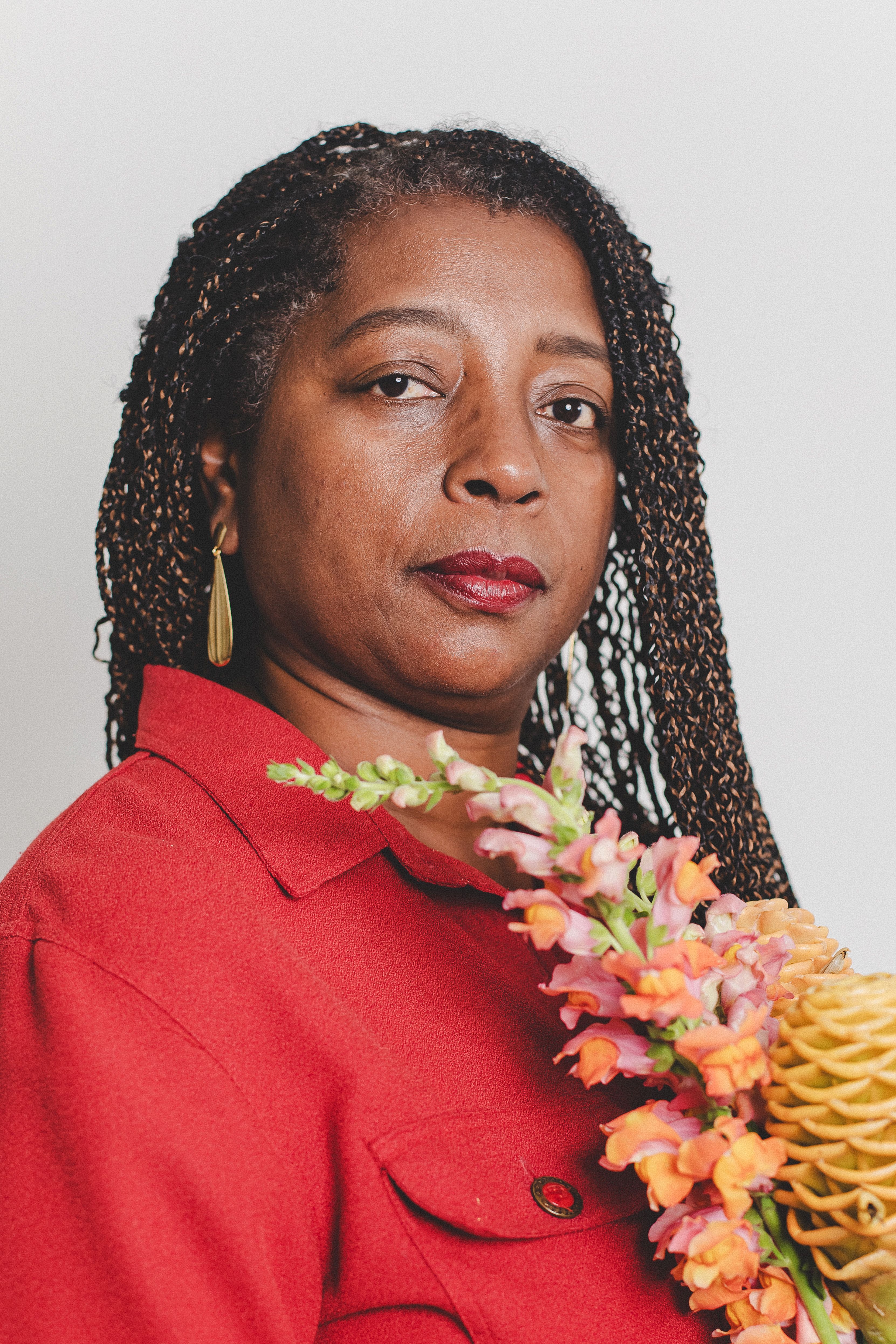 Elegant portrait of a woman in a red outfit holding vibrant flowers against a neutral background.
