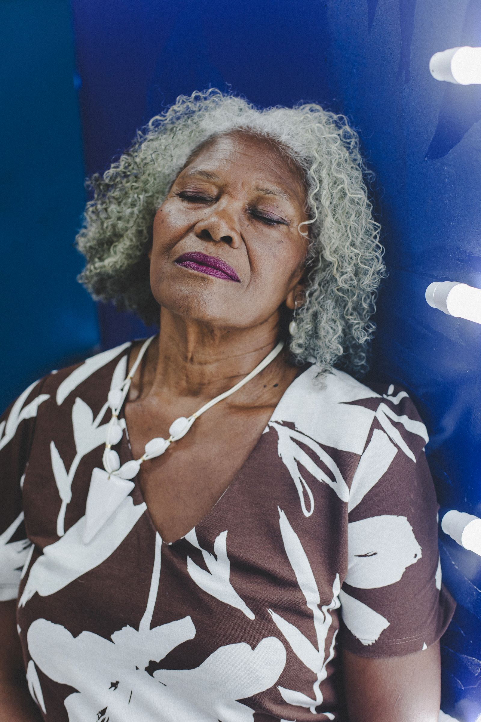 An older Black woman with gray curly hair rests with her eyes closed, lit by soft window light. Cataracts are common with age and are reversible with a brief outpatient surgery.