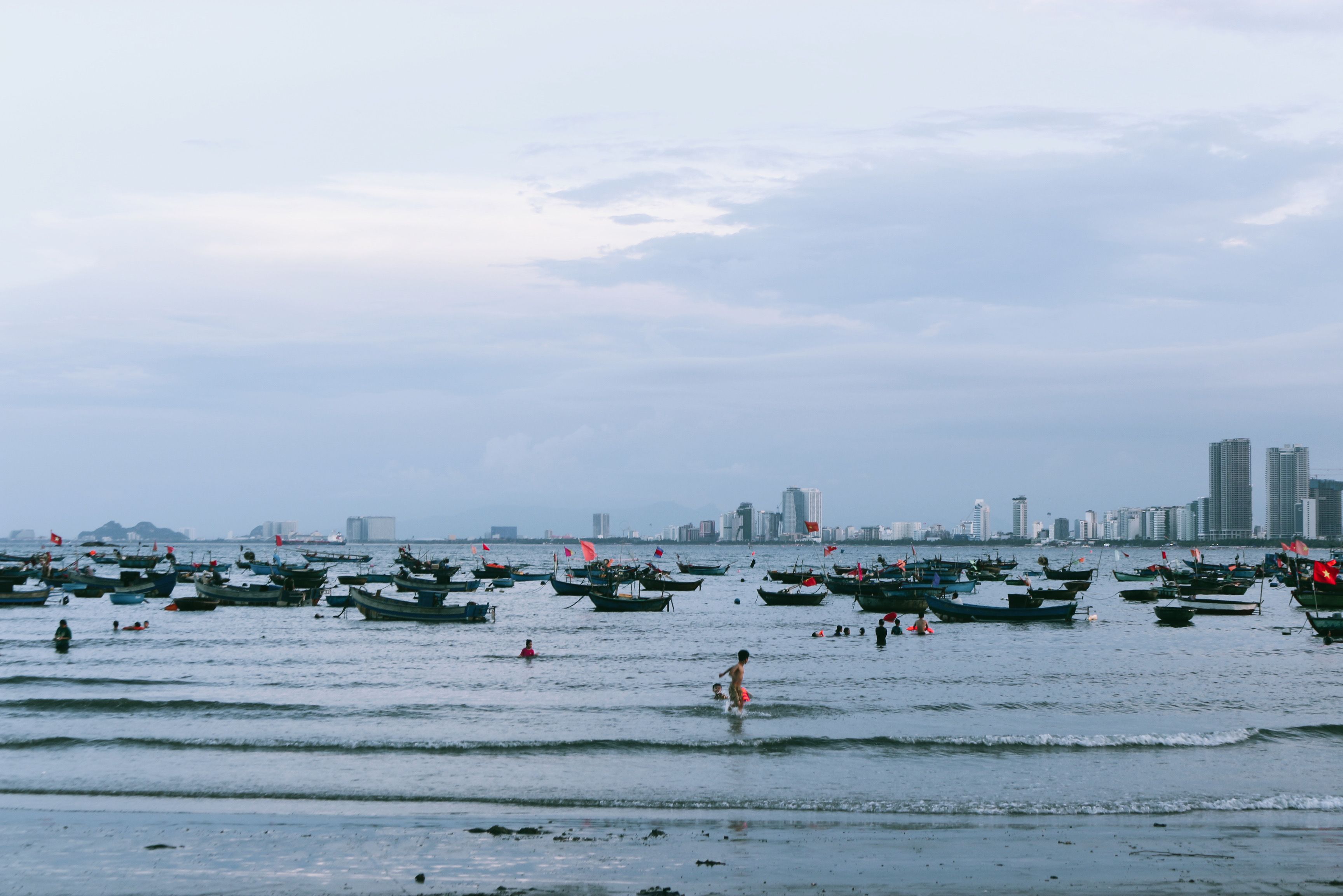 Peaceful beach view in Da Nang, Vietnam with boats dotting the sea and city skyline in the background.