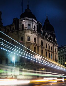 Long exposure of a historic building with dynamic light trails in a city at night.