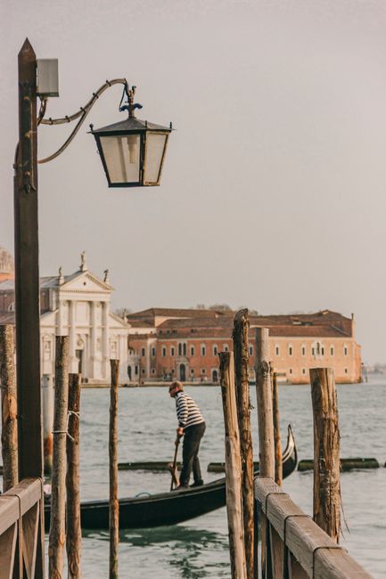 A gondolier in Venice's iconic canals with historical architecture in the background during daylight.