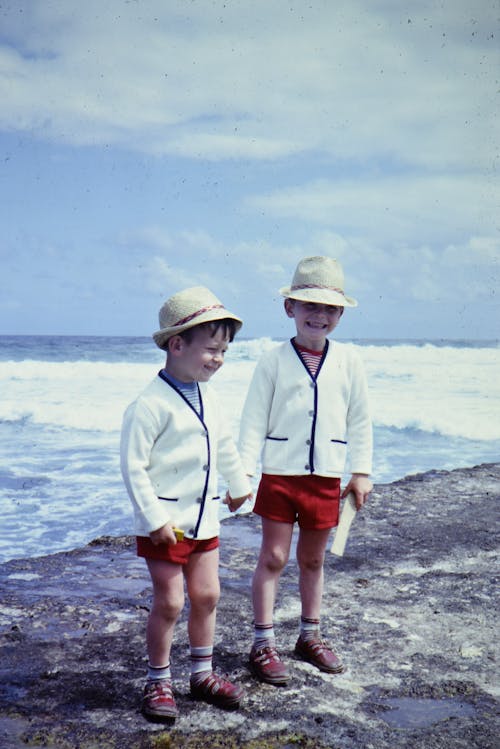 Dos Muchachos En Suéteres Blancos Y Pantalones Cortos Rojos De Pie En La Playa