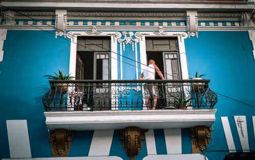 Free Vibrant blue facade with a man standing on an ornate balcony in Trujillo, Peru. Stock Photo