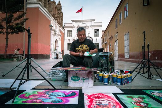 A street artist creates vibrant paintings in front of a historic building in Trujillo, Peru.