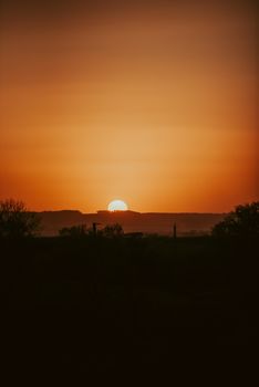 A dramatic sunset casting a warm glow over a silhouetted landscape.