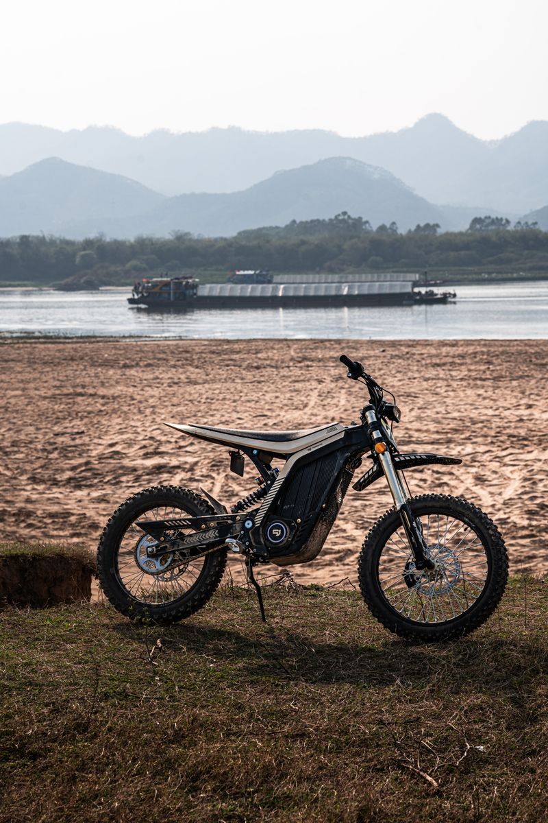 Electric dirt bike parked on a riverside with mountains