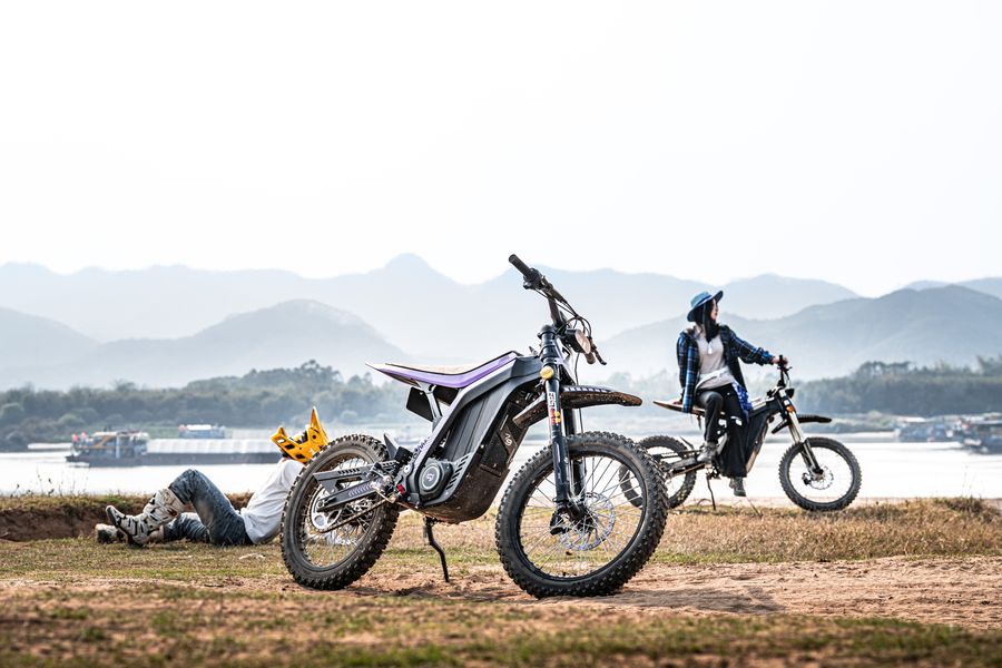 Riders hanging out with electric dirt bikes by the river