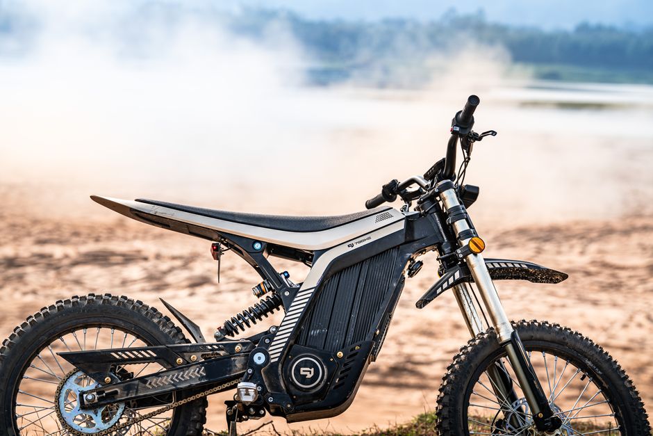 Close-up of an electric dirt bike on a sandy terrain with misty background, showcasing eco-friendly innovation.