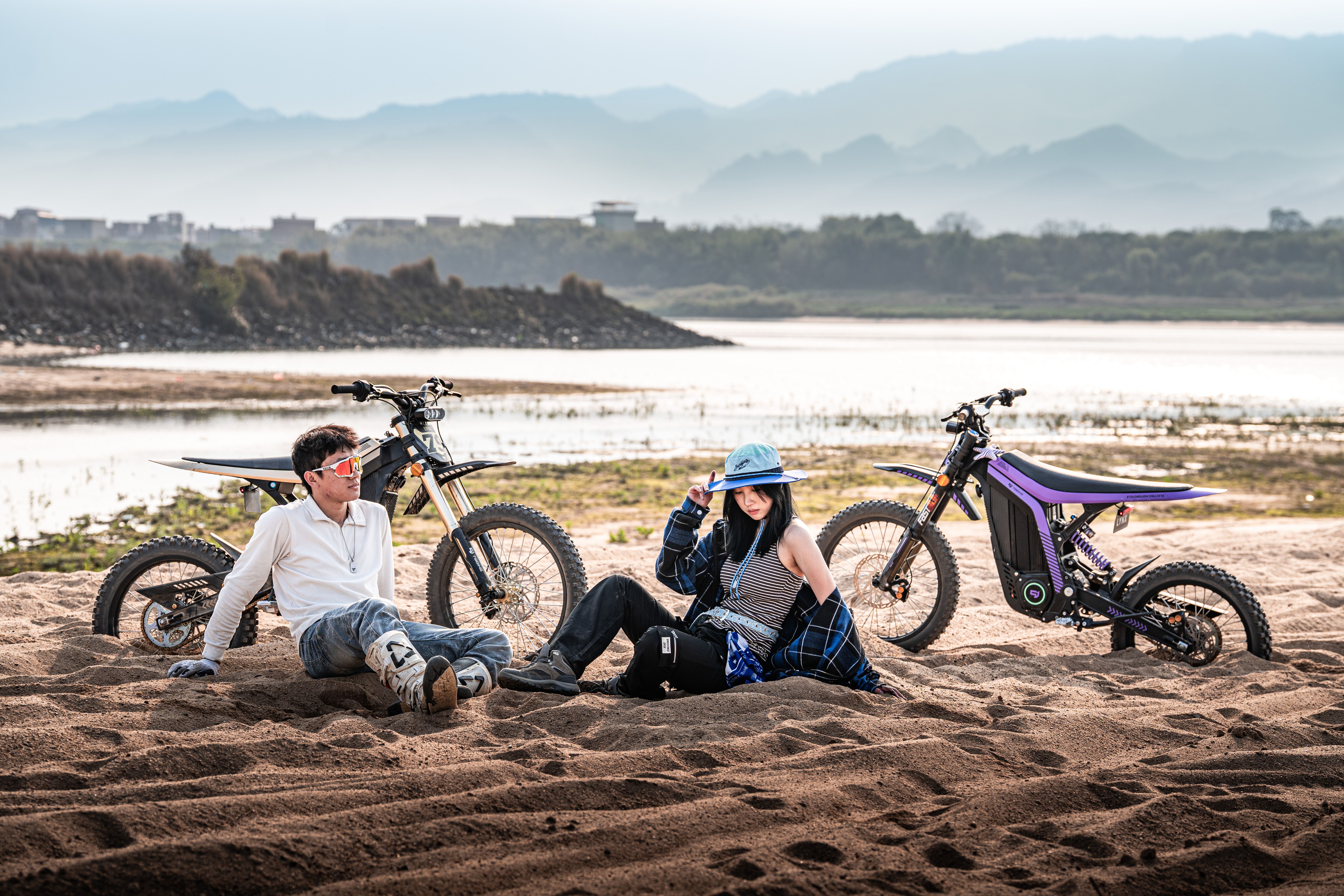 Man and woman on a sandy riverbank with electric bikes.