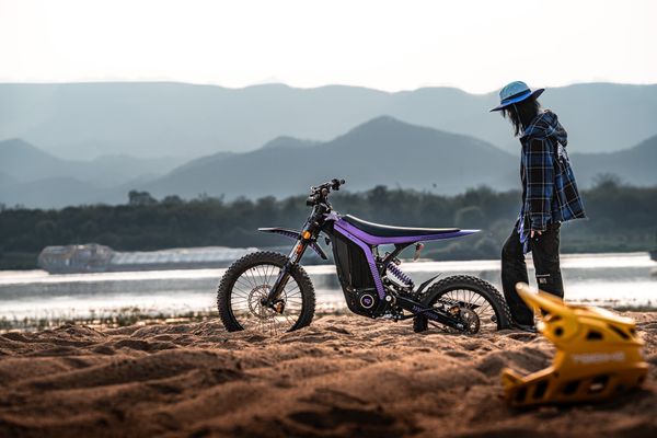 Rider standing with an electric dirt bike at sunset