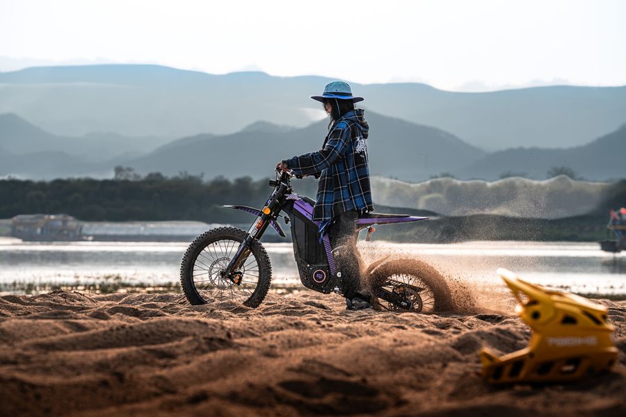 Rider roosting sand on an electric dirt bike at sunset