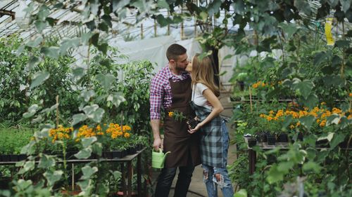 Free Couple kissing in a vibrant greenhouse surrounded by colorful flowers. Stock Photo