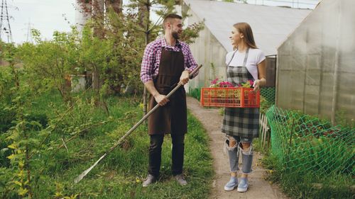 Free Two young gardeners sharing tasks outside a greenhouse, tending plants. Stock Photo