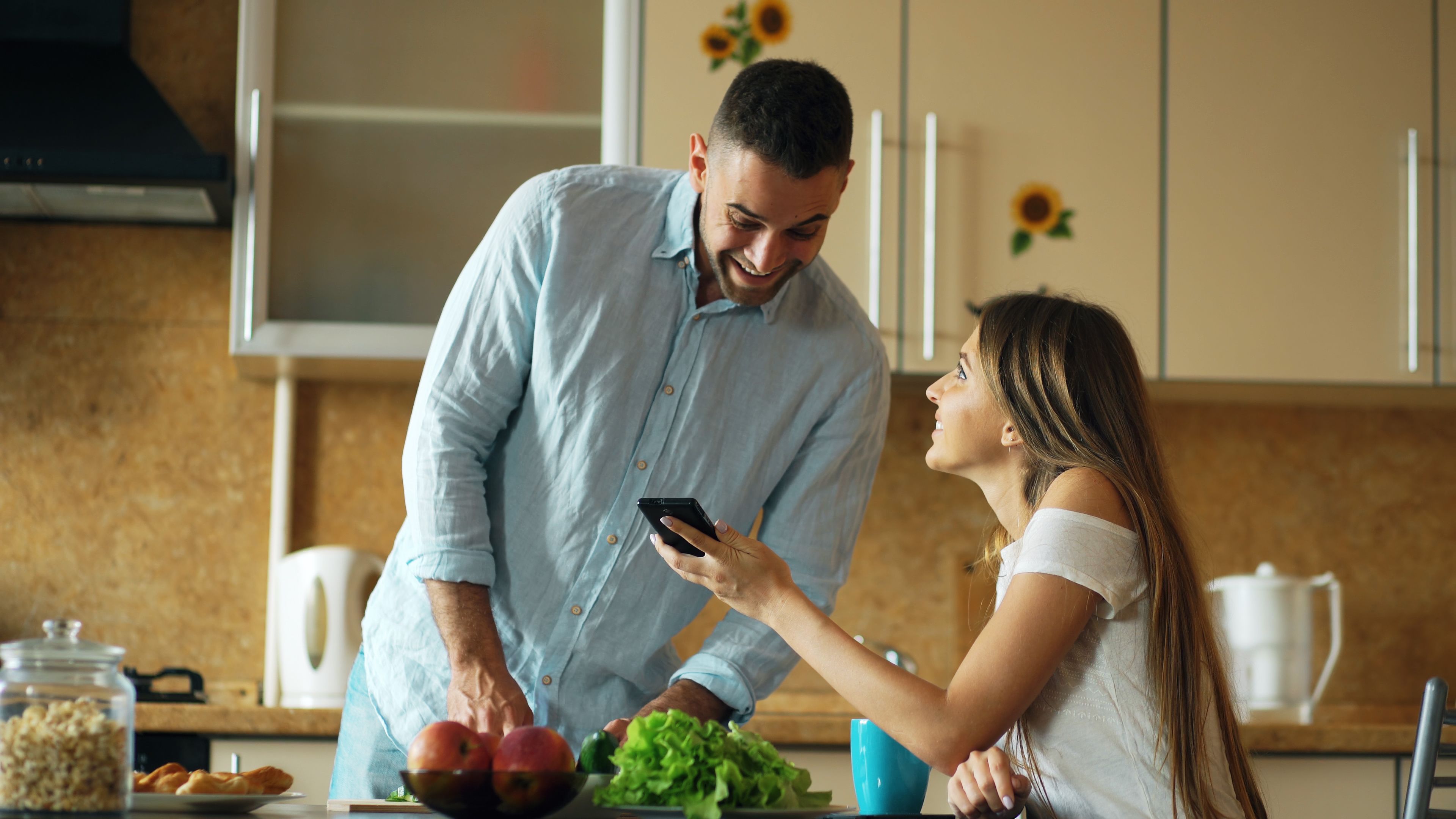 A happy couple in a bright kitchen, sharing laughter and preparing fresh food.