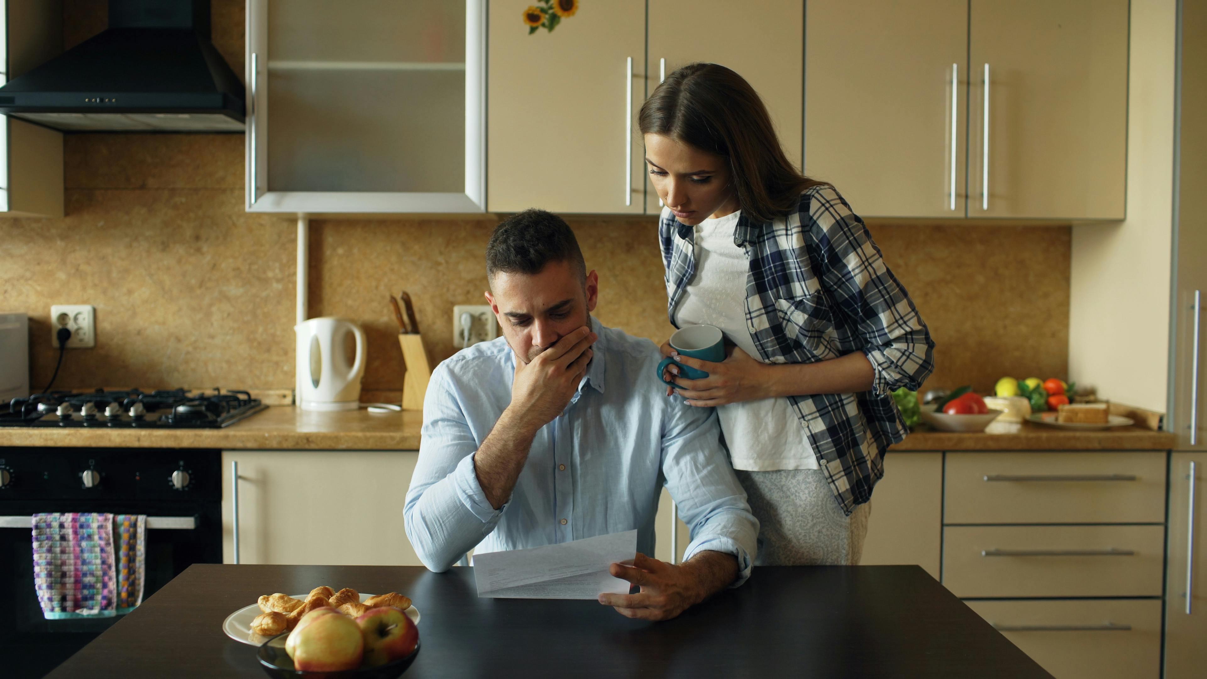 Concerned couple reviewing financial document in modern kitchen setting.