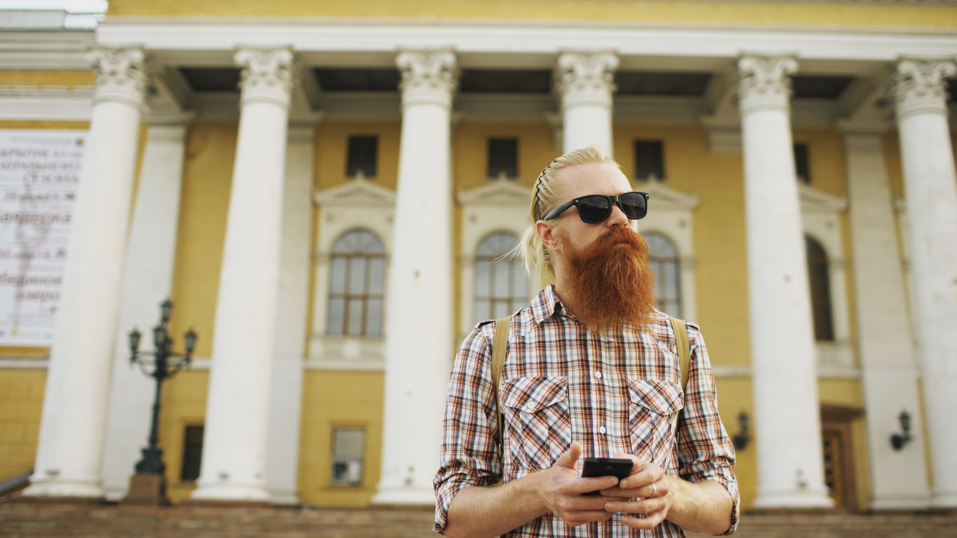 Stylish man with sunglasses and phone in front of a neoclassical building.