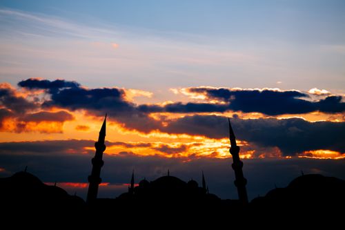 Free A dramatic silhouette of a mosque with minarets against a vibrant, colorful sunset sky. Stock Photo