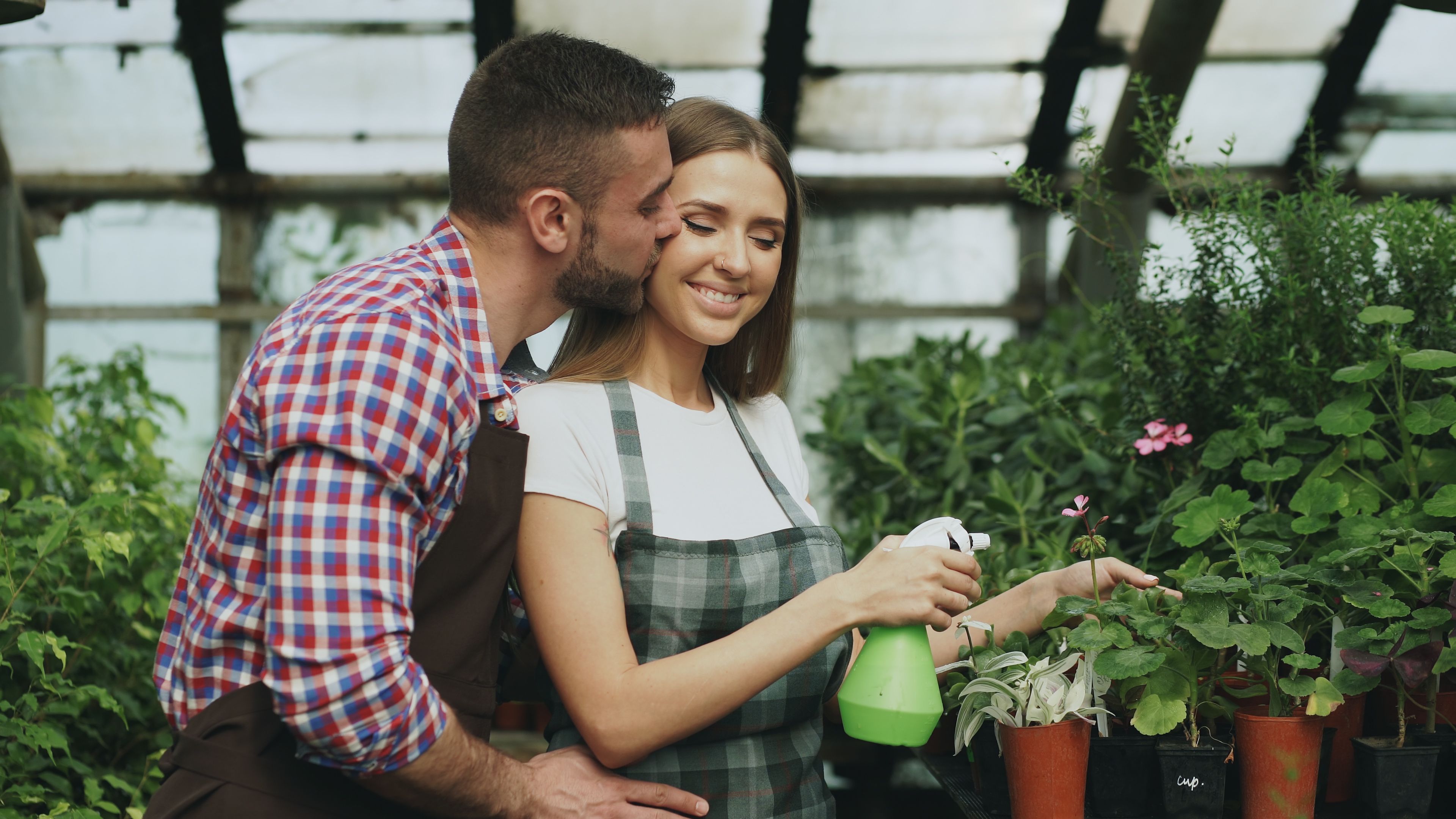 Couple joyfully caring for plants in greenhouse, romantic interaction.
