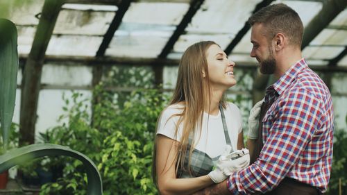 Free Happy couple sharing a moment in a lush green greenhouse setting. Stock Photo