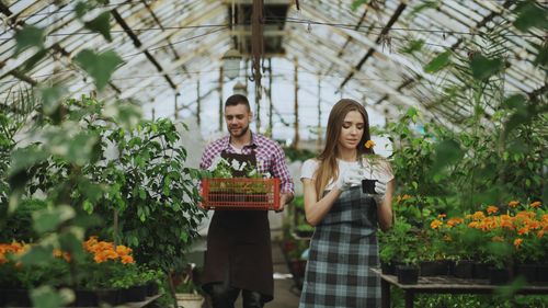 Free Two gardeners tending to plants in a greenhouse, surrounded by lush greenery and vibrant blooms. Stock Photo