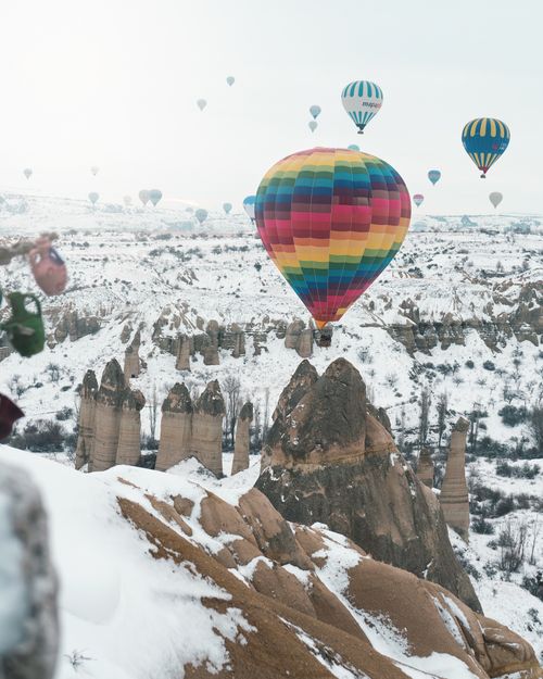 Free Hot air balloons soaring over snow-covered rock formations in Cappadocia, a scenic winter adventure. Stock Photo