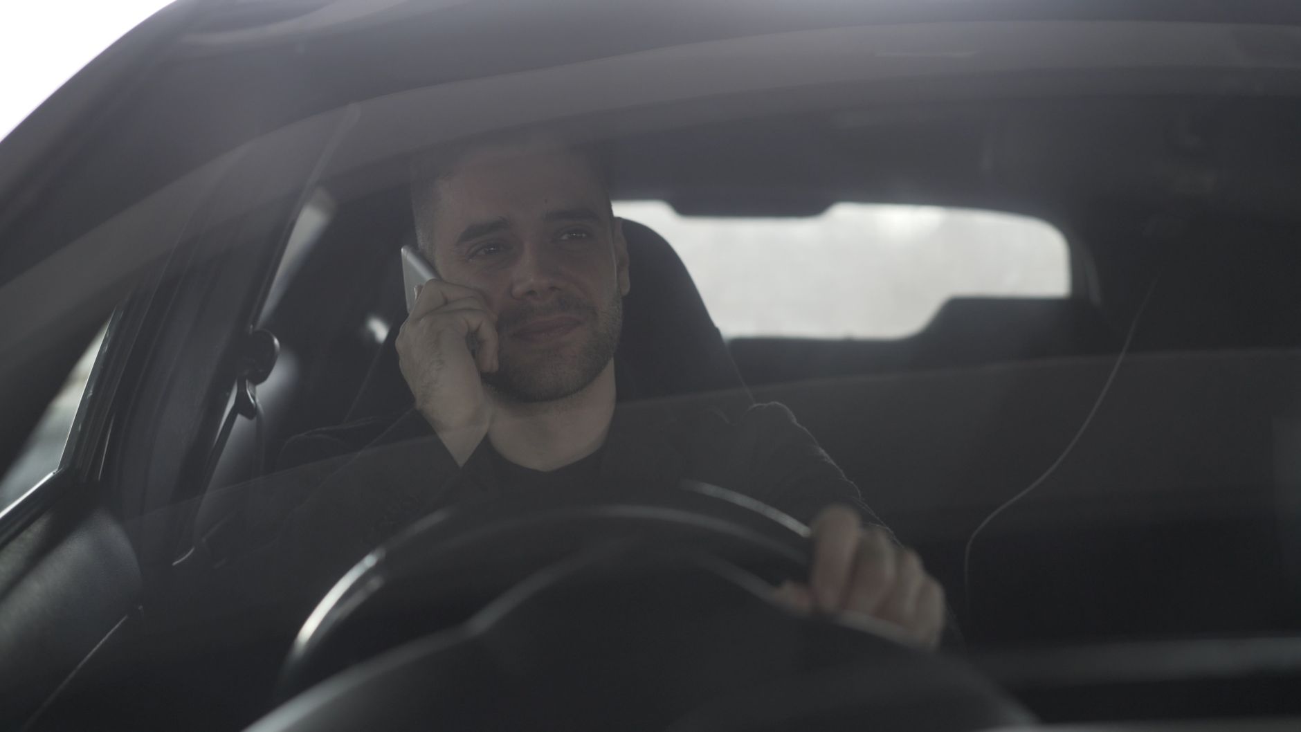 Man talking on mobile phone while driving, seen through car windshield.