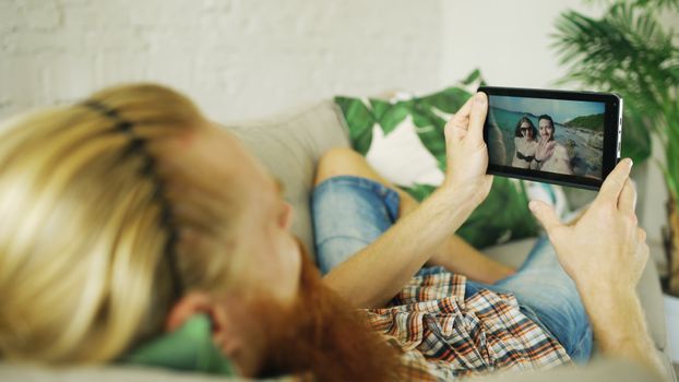 A person lounging on a couch viewing vacation photos on a tablet, enjoying leisure time indoors.