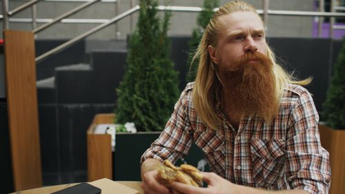 Free A man with a long red beard enjoying a sandwich at an outdoor cafe. Stock Photo
