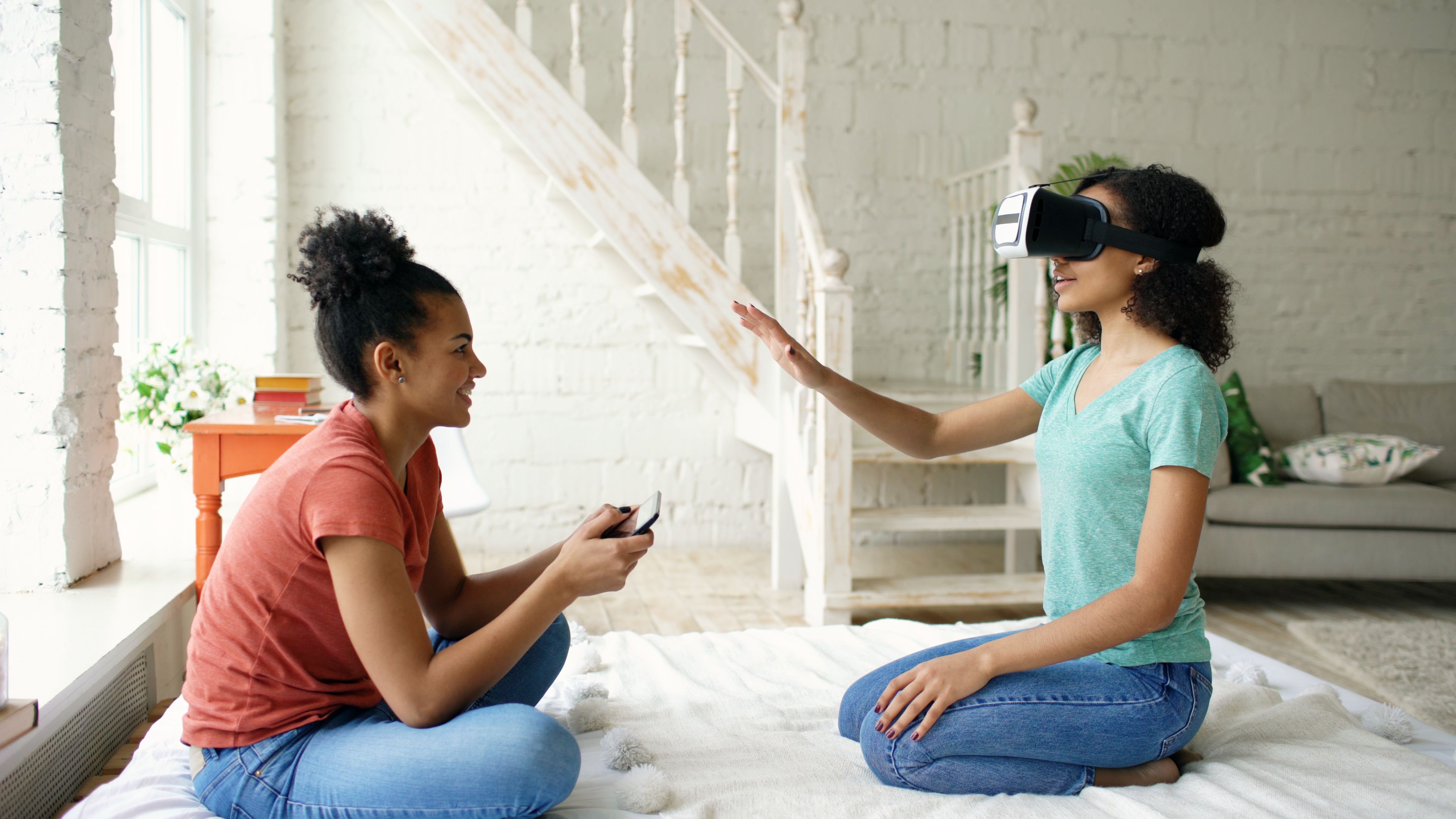 Two women enjoying virtual reality at home with a headset and smartphone.