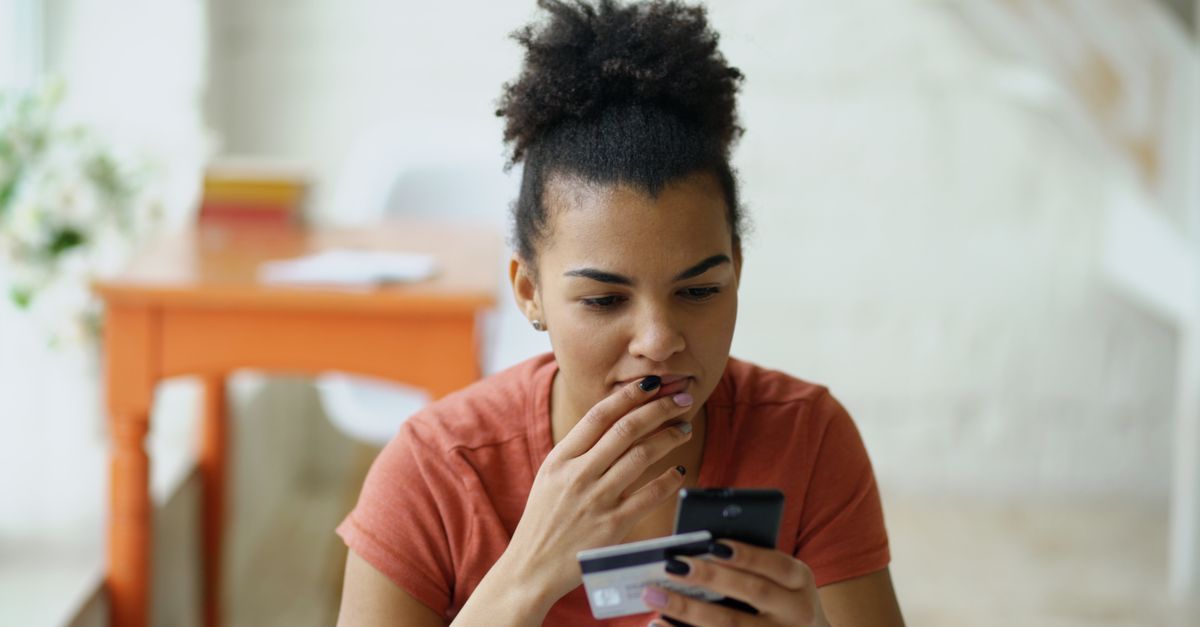 person looking at phone in dimly lit room with credit card in hand, late night shopping