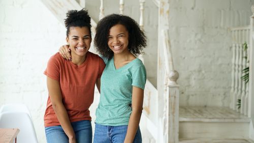 Free Two happy young women smiling indoors, embracing in casual outfits. Stock Photo
