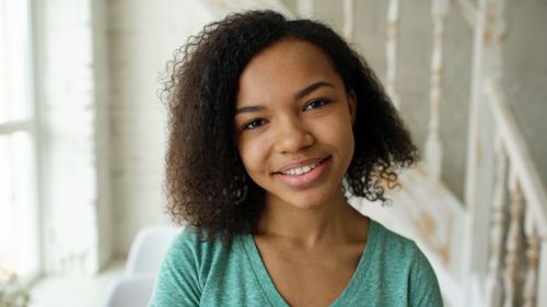 Free A bright and cheerful portrait of a young woman with curly hair smiling indoors. Stock Photo