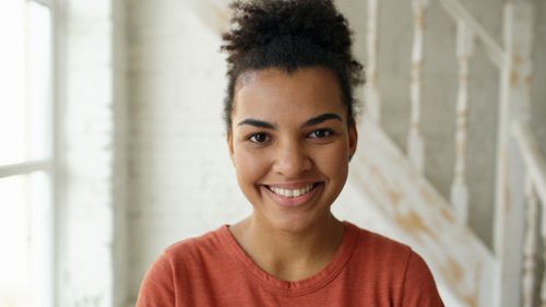 Free Portrait of a smiling woman indoors with natural light and a soft, neutral background. Stock Photo