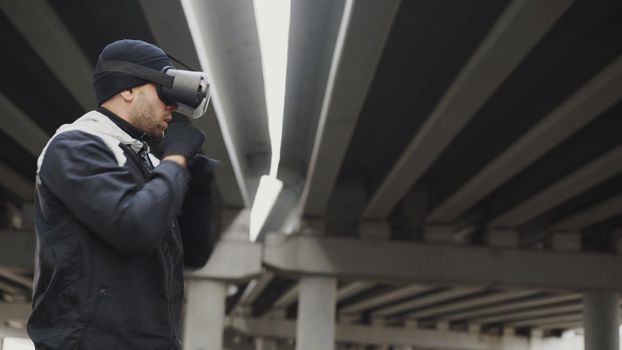 A man wearing VR headset practicing boxing outdoors under a bridge.