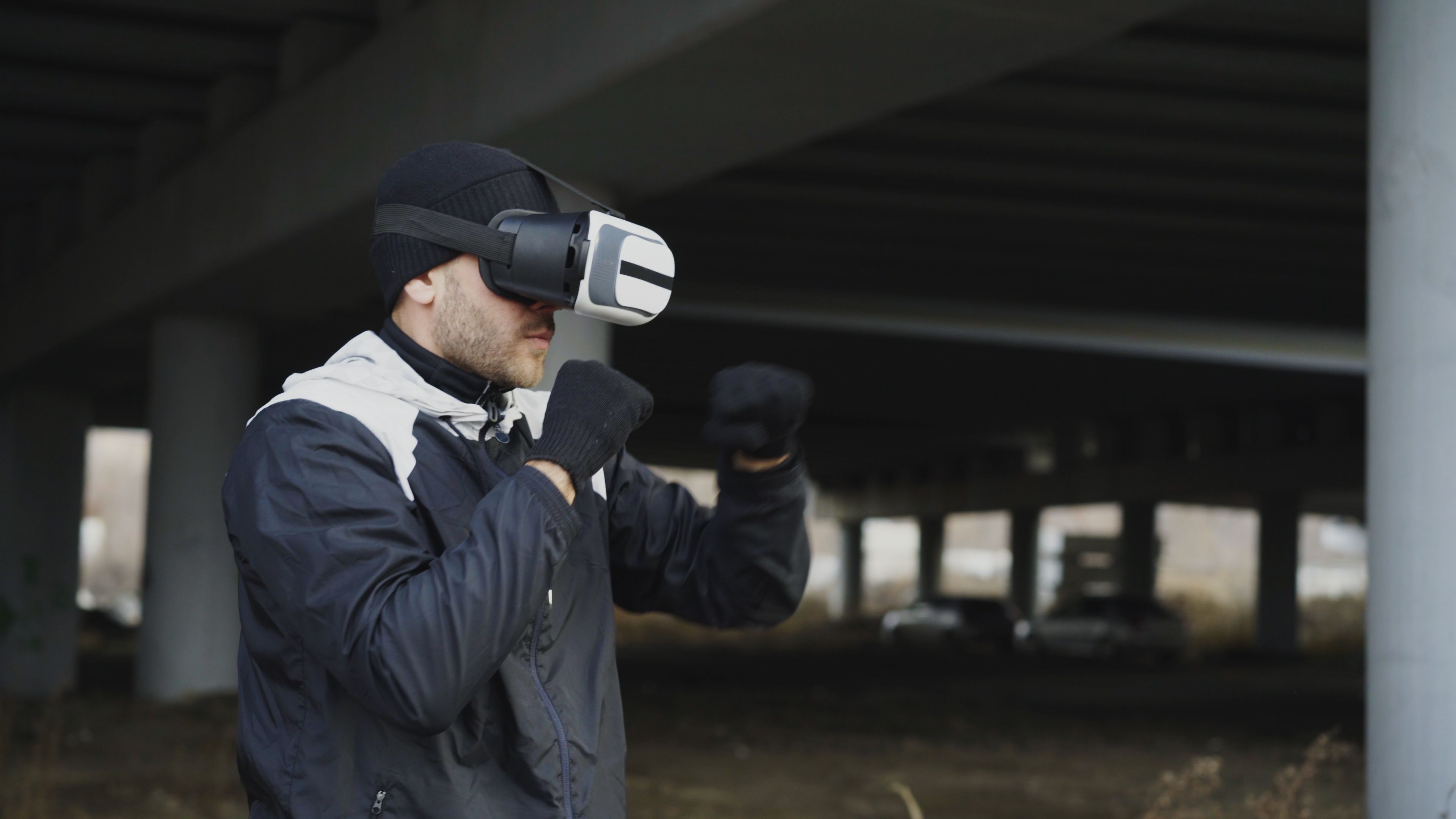Man practicing boxing with VR headset under a bridge outdoors.