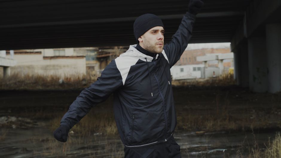 man exercises under a bridge, wearing warm athletic clothing.