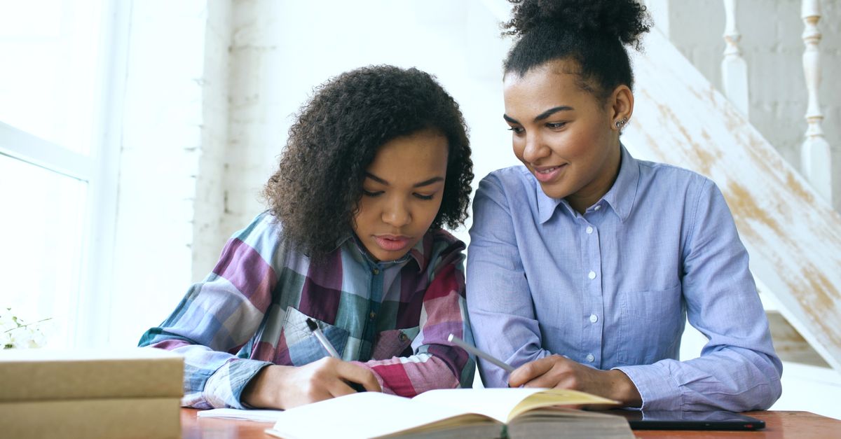 Teen studying with an adult at a home table, focusing on learning and education.
