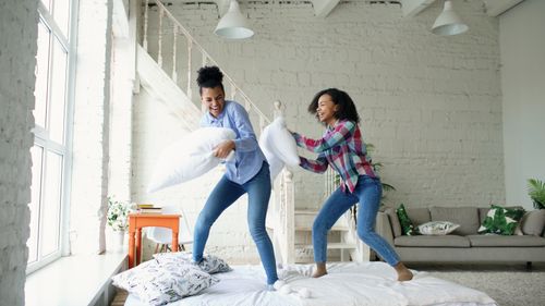 Free Two young women enjoying a playful pillow fight in a bright, modern living room. Stock Photo