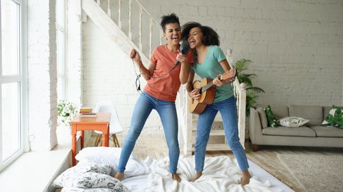 Free Two friends enjoy singing and playing guitar together in a cozy living room setting. Stock Photo