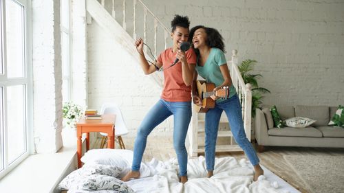 Free Two friends joyfully sing and play guitar in a bright, cozy room, exuding happiness and friendship. Stock Photo