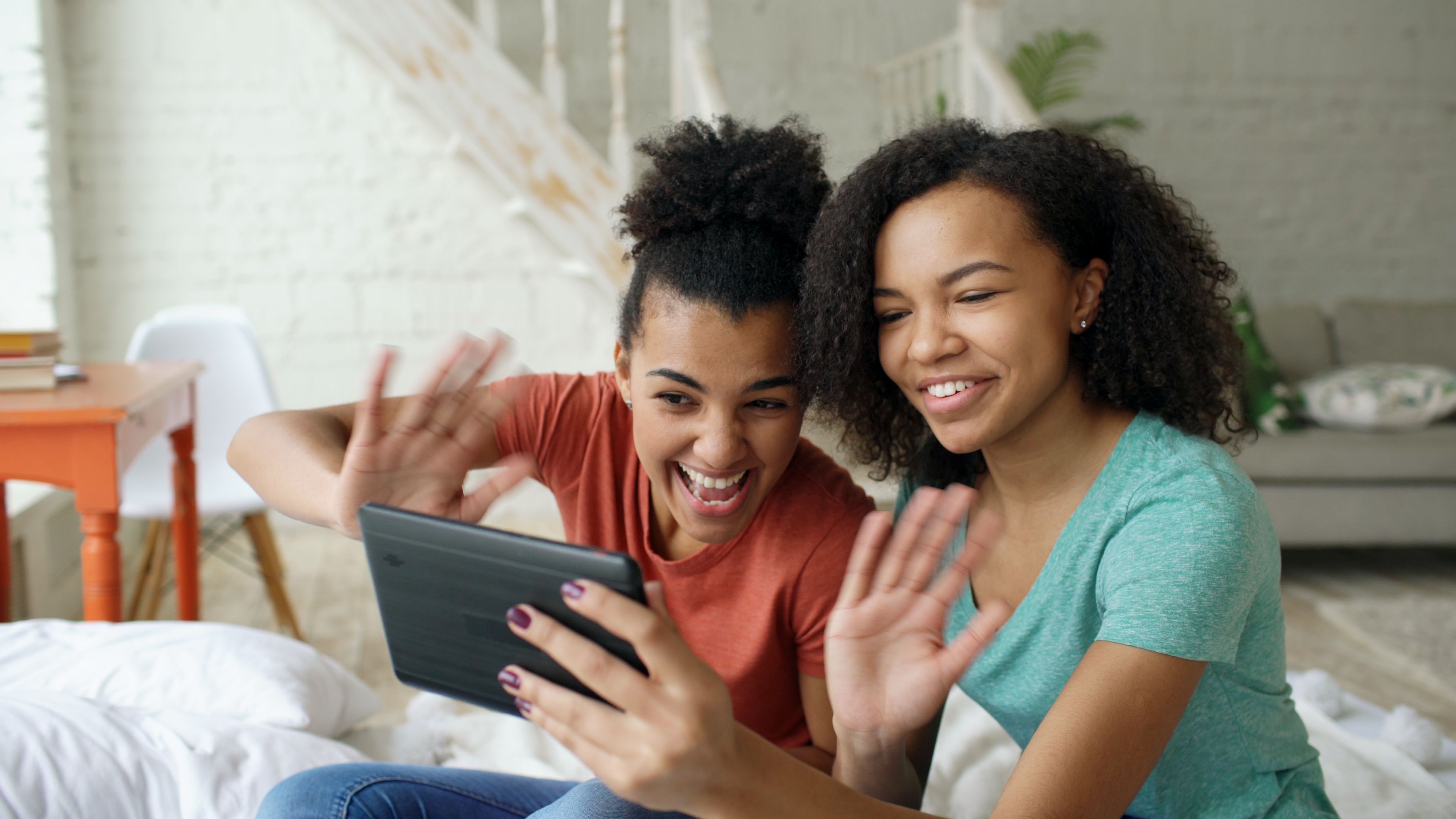 Two teenagers excitedly video chatting on a tablet indoors.