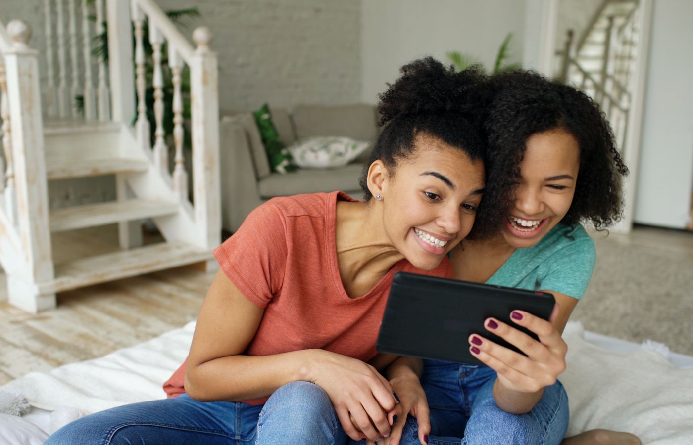 Two young women laughing and enjoying on a tablet, indoors, relaxed atmosphere.