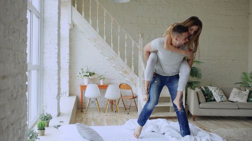 Free A joyful couple plays together in a modern, sunlit living room with a cozy design and bright atmosphere. Stock Photo