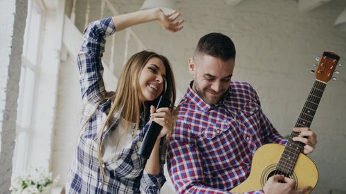 Free Joyful couple enjoying music indoors with guitar and microphone. Stock Photo