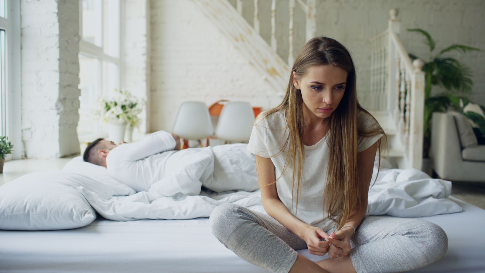 A person sitting on a bed looking thoughtful