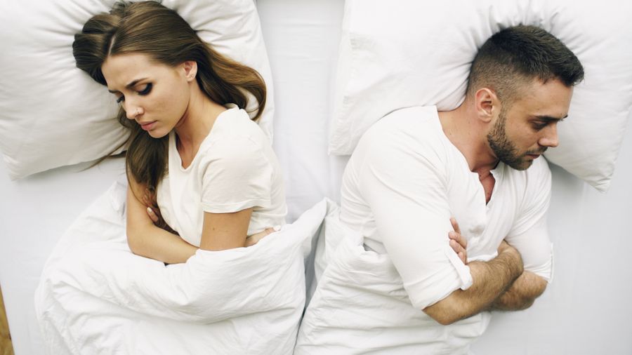 Couple lying apart in bed showing signs of a toxic relationship